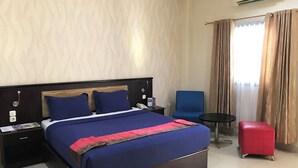 Una habitación de hotel con una cama grande, una mesita pequeña, una silla y un reposapiés rojo.