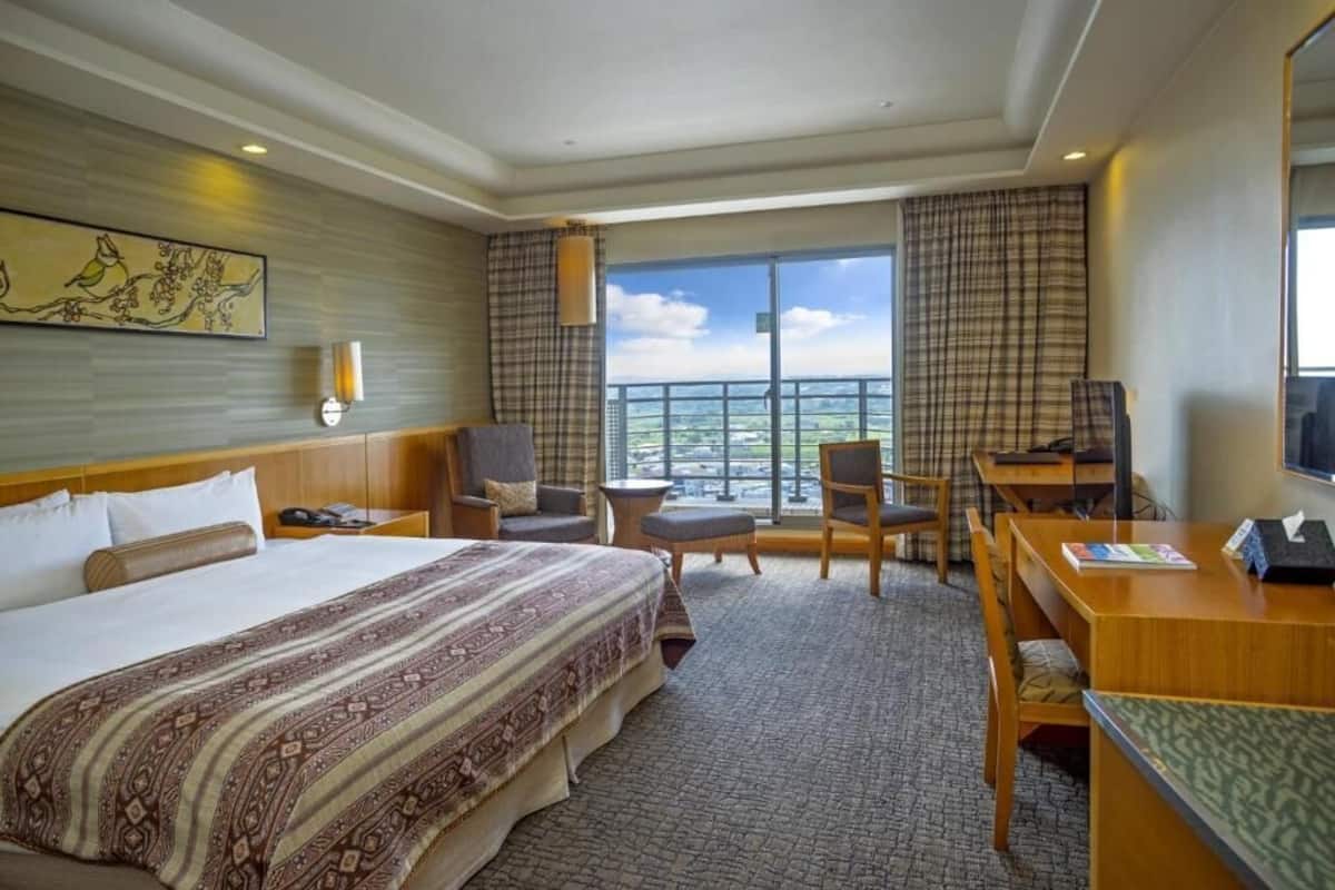Habitación de hotel con una cama grande, un escritorio, una silla, una mesita y vistas a la ciudad.