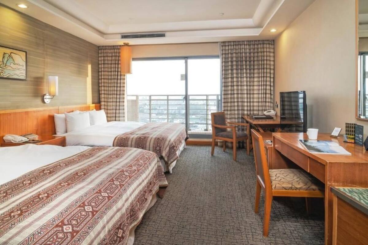 Habitación de hotel con dos camas, un escritorio, una silla, un televisor y una ventana con cortinas.