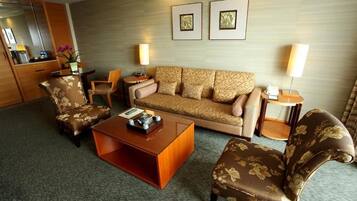 Habitación de hotel con sofá, dos sillones, una mesita de centro, una mesita auxiliar y una lámpara. Se observa un espejo, una pequeña mesa con un florero y dos cuadros en la pared.