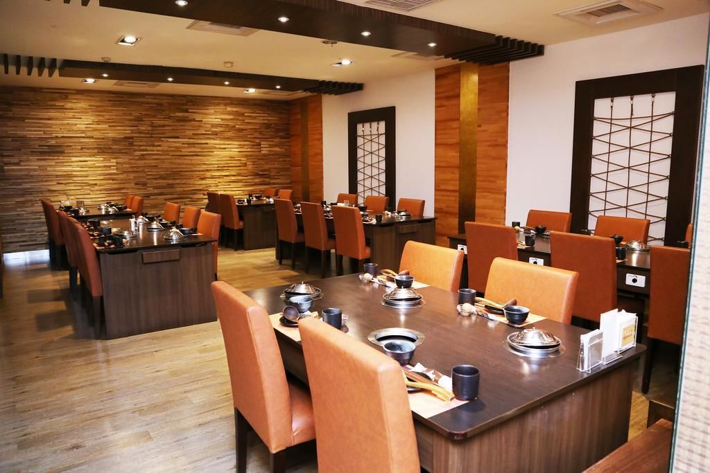 A restaurant with a long wooden table set for dining, surrounded by orange chairs.