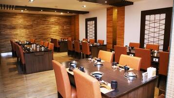 A restaurant with a long wooden table set for dining, surrounded by orange chairs.