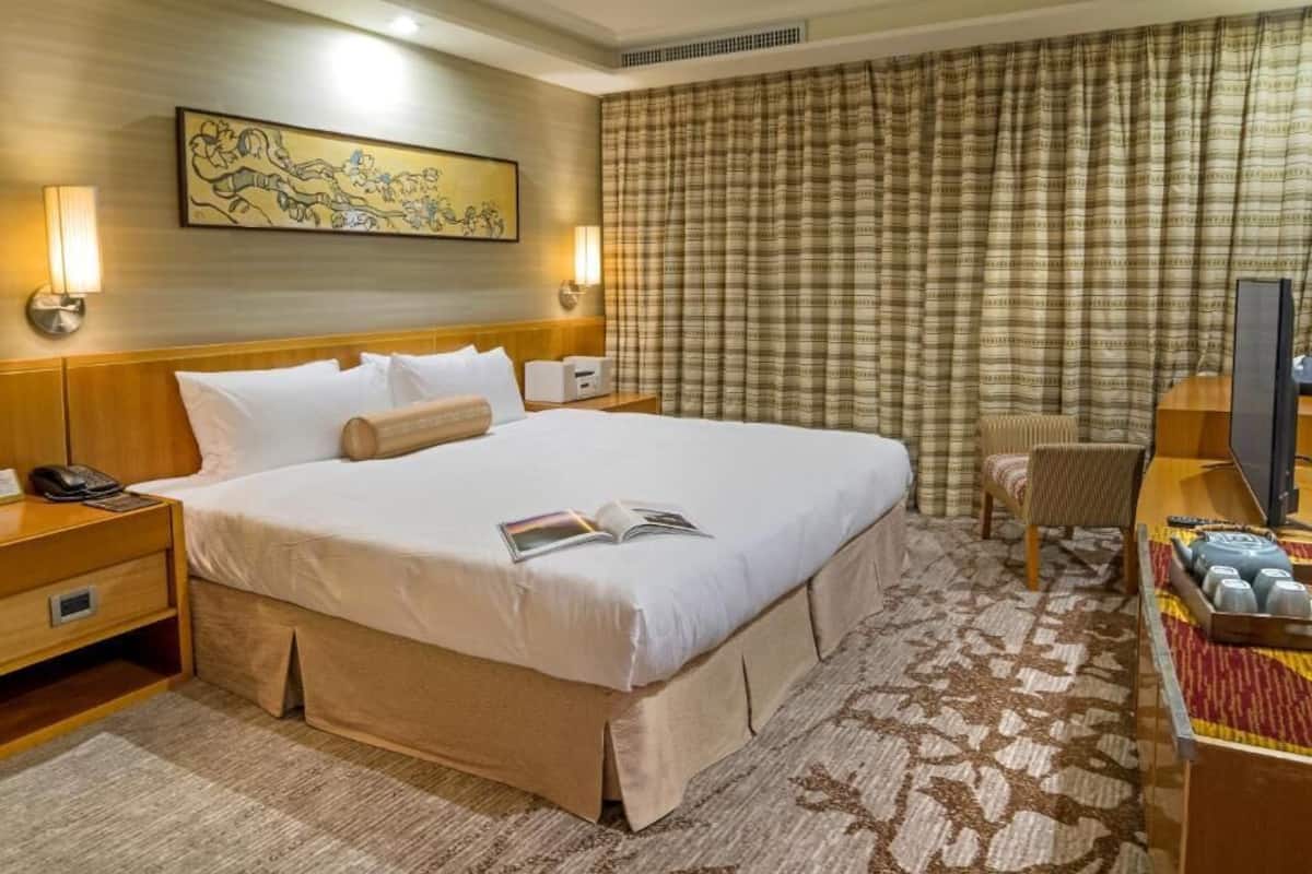 Habitación de hotel con una cama grande, una mesita de noche con lámpara, televisión y una pequeña mesa con una bandeja de vasos.