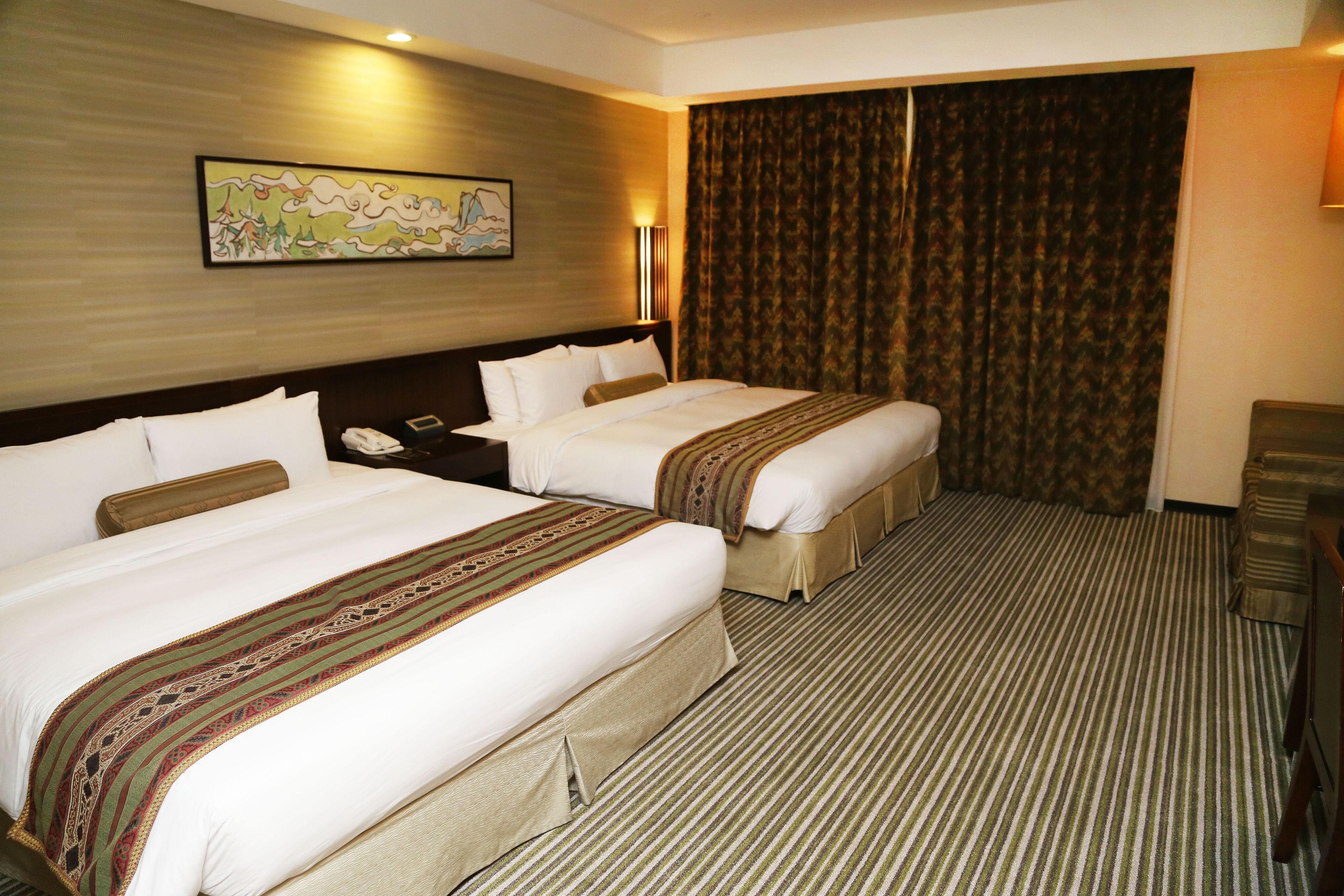 Habitación de hotel con dos camas, cabecero, mesita de noche con teléfono, una obra de arte colgada en la pared y un amplio ventanal con cortinas.