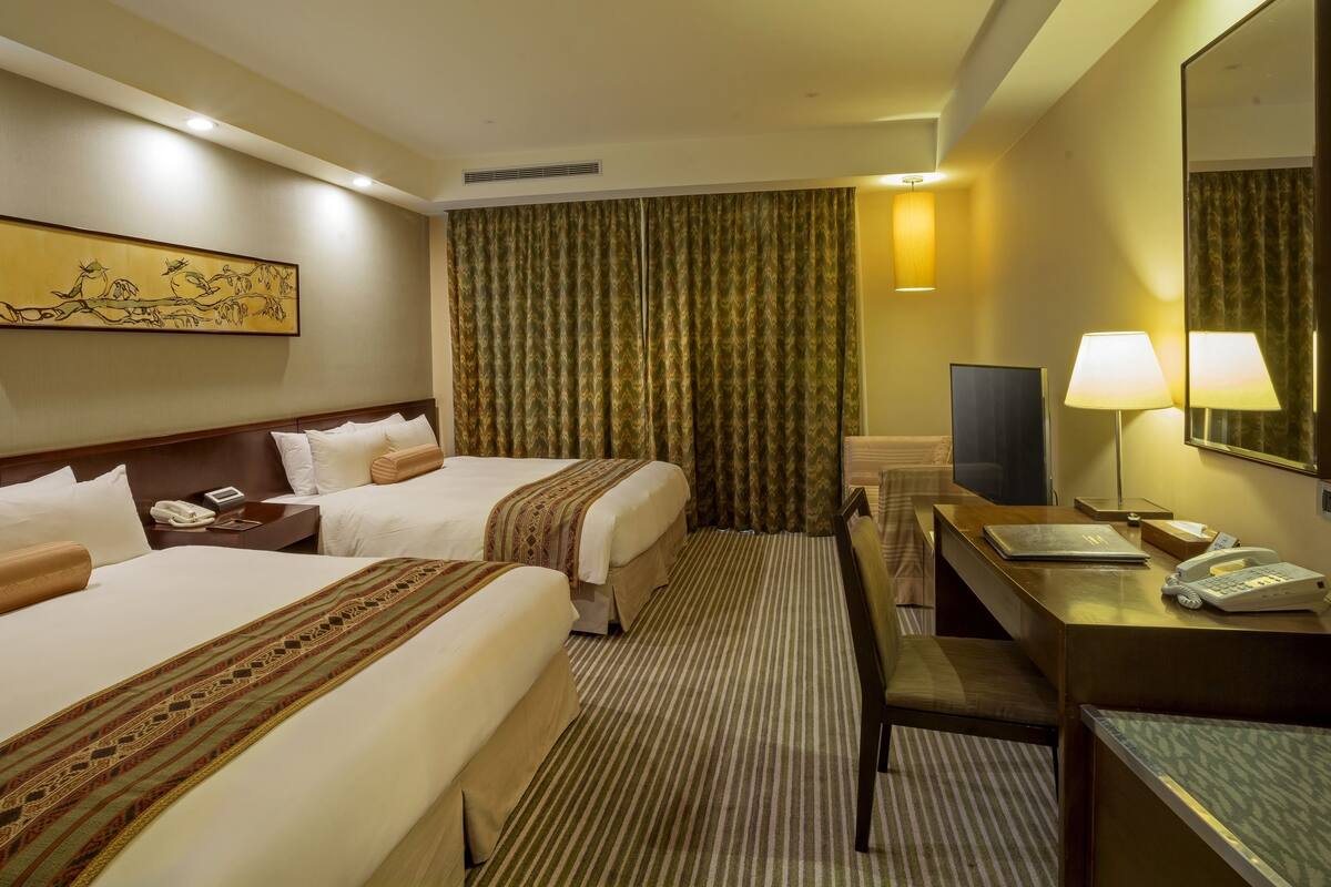 Habitación de hotel con dos camas, un escritorio, un teléfono, una computadora portátil y un televisor.