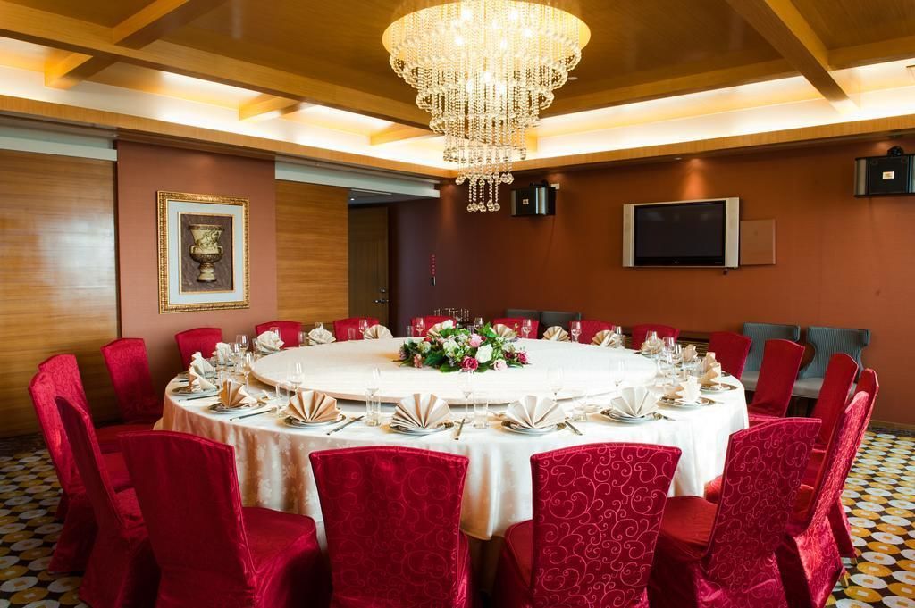 A conference room with a round table, red chairs, a chandelier, and a television on the wall.