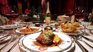 Una mesa de comedor formal adornada con varios platos de comida, copas de vino y una botella.