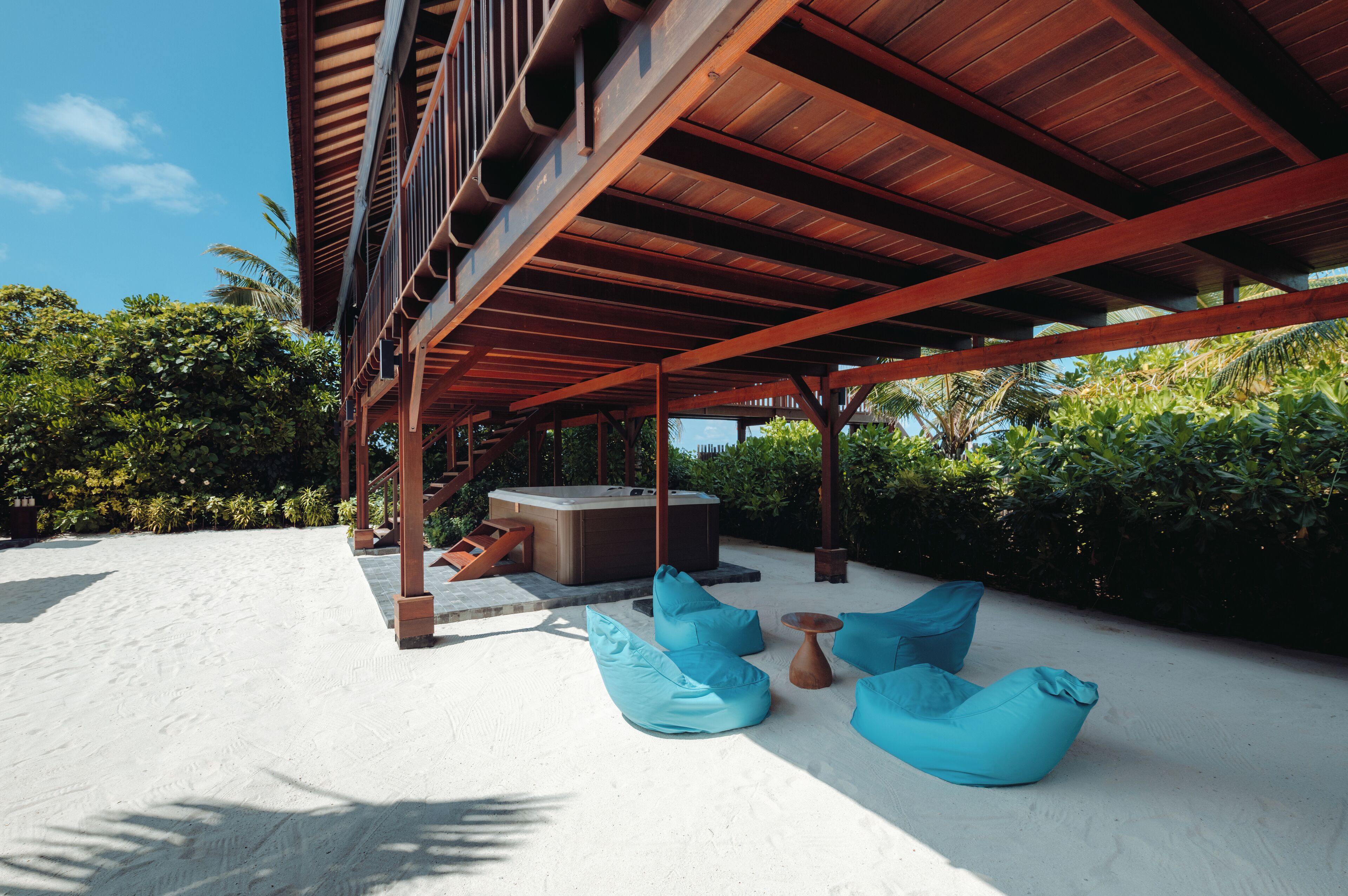 Un espacio al aire libre techado con un jacuzzi, puffs azules y una terraza de madera.