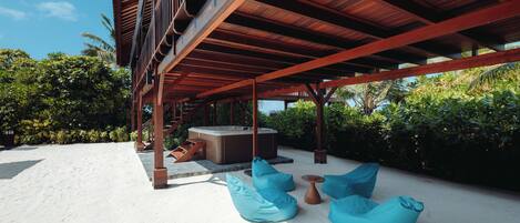 Un espacio al aire libre techado con un jacuzzi, puffs azules y una terraza de madera.