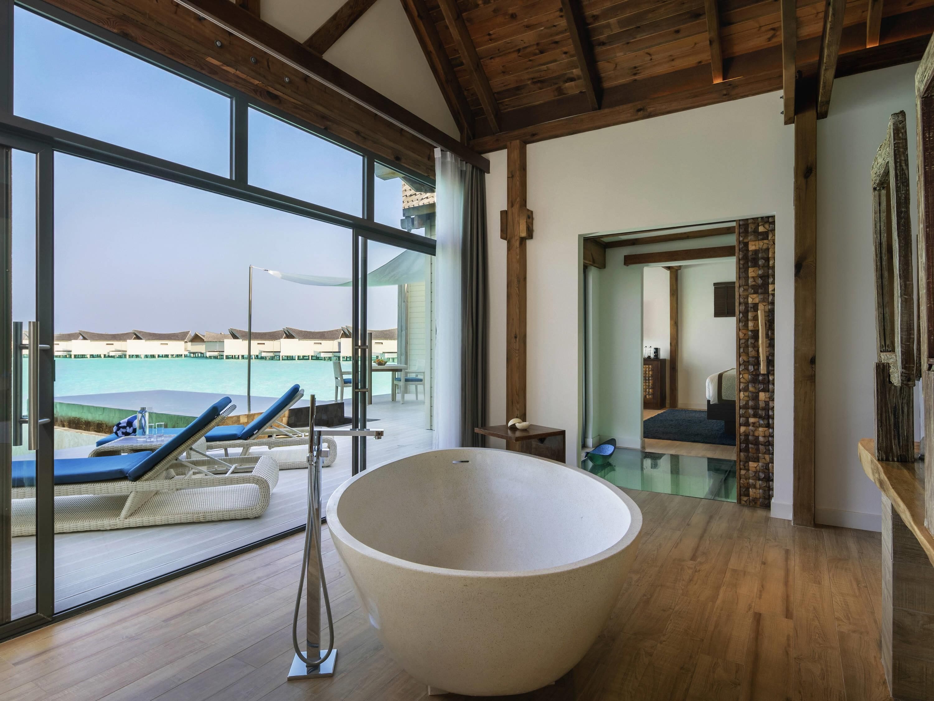 A modern room with a large bathtub, wooden flooring, and large windows overlooking a pool area.
