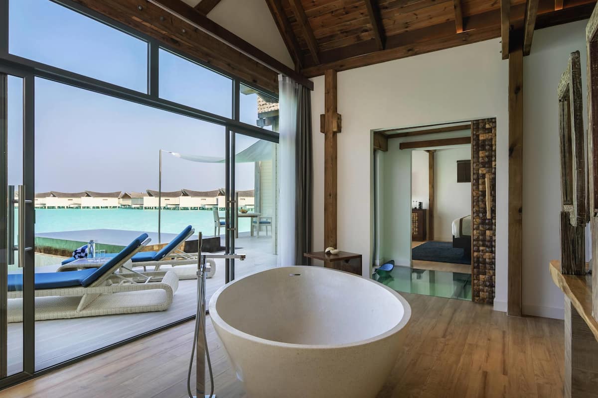 A modern room with a large bathtub, wooden flooring, and large windows overlooking a pool area.
