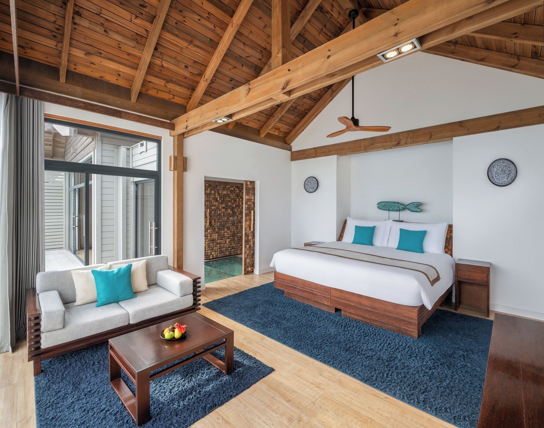 Un dormitorio amplio con una cama grande, techo de madera y vista a una piscina a través de un ventanal.