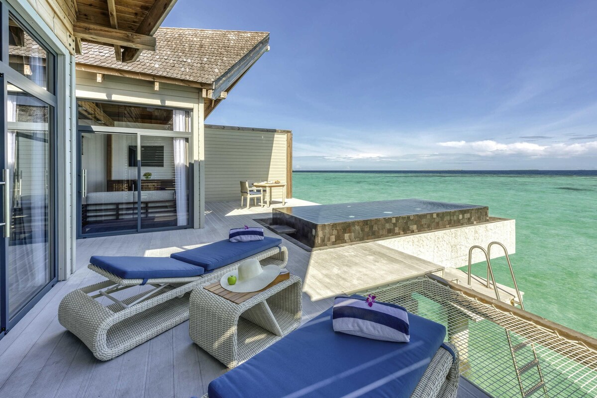 A modern outdoor lounge area with wicker furniture, a glass door entrance, and a view of the ocean.