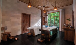 A spa room with two massage tables, wooden furniture, a large window with a view of greenery, and hanging pendant lights. - Kuredhivaru Resort & Spa Maldives by Accor (Kuredhivaru)
