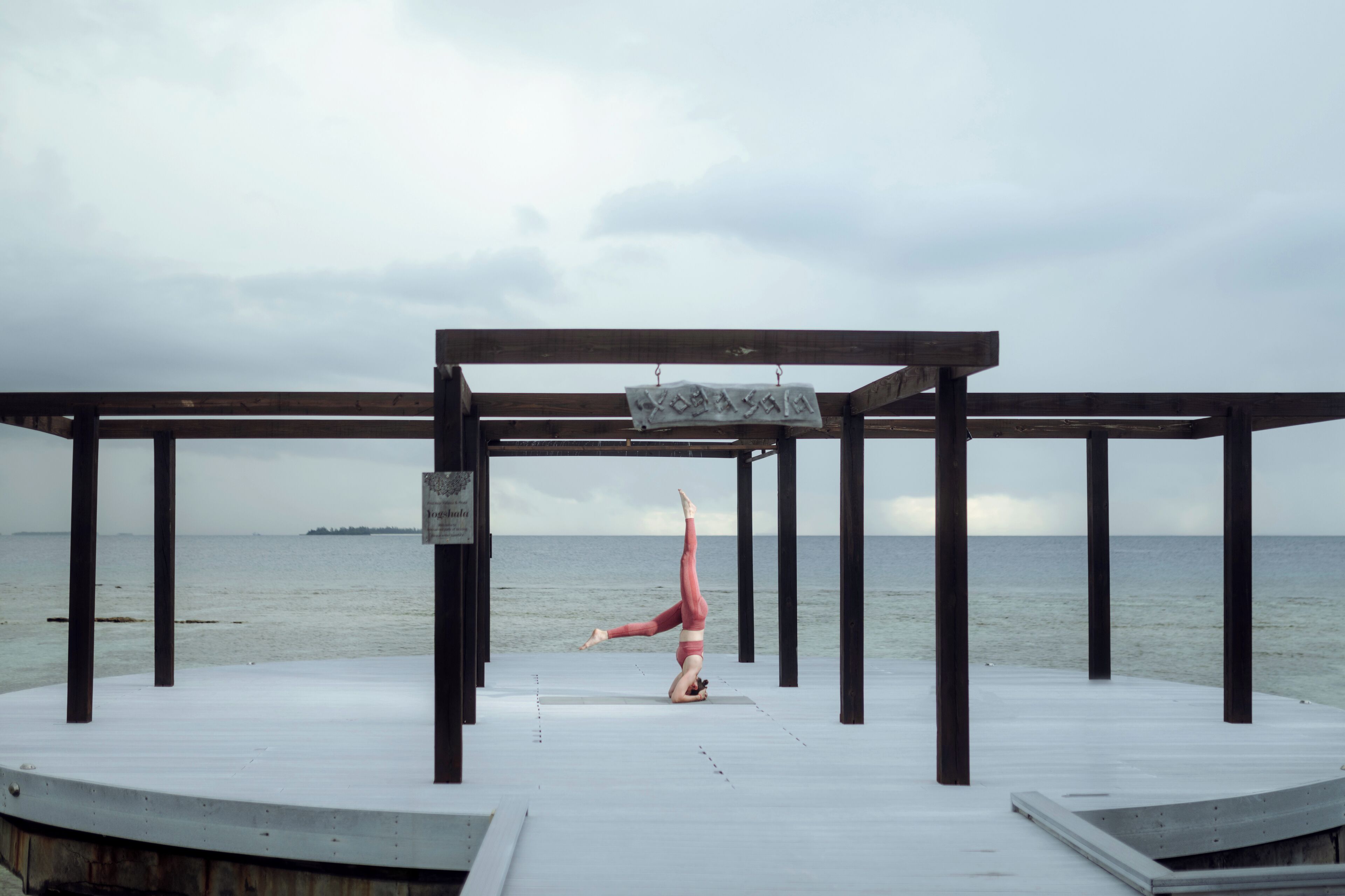 Iemand doet een handstand op een houten terras, met uitzicht op zee.