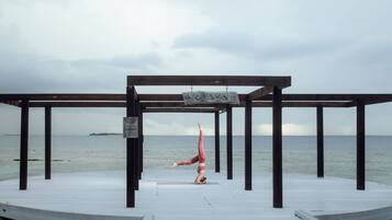 Iemand doet een handstand op een houten terras, met uitzicht op zee.