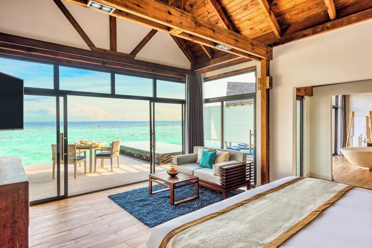 Ruime kamer met een groot schuifglasraam dat leidt naar een balkon met uitzicht op de oceaan.
