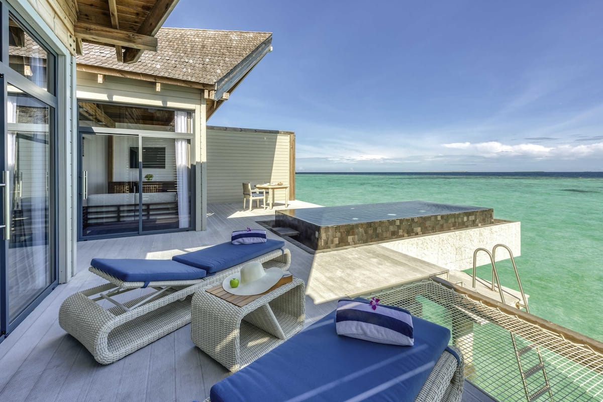 A modern outdoor lounge area with wicker furniture, a glass door entrance, and a view of the ocean.