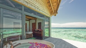 Een modern overloopzwembad met jacuzzi, omgeven door een houten terras en glazen wanden met uitzicht op de oceaan.
