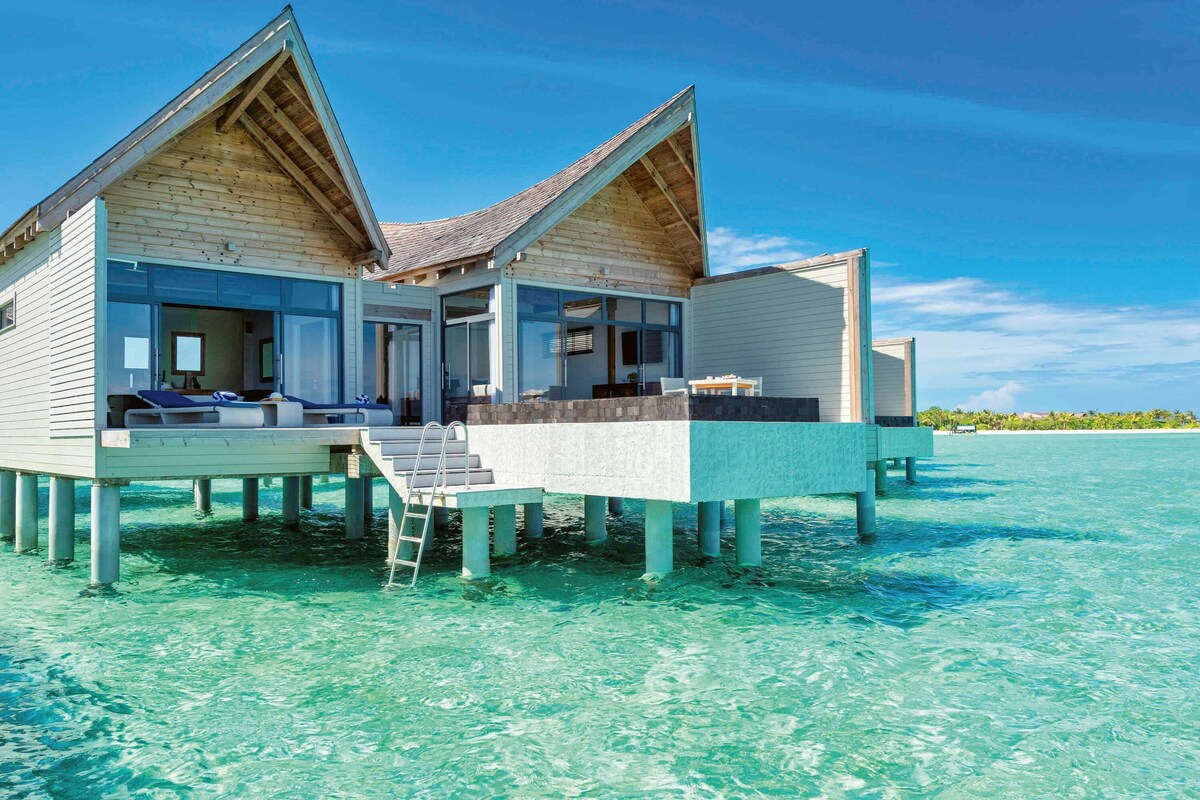 Een twee verdiepingen tellende bungalow op palen, met balkon, helderblauw water en een houten gevel.
