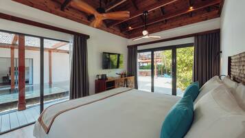 A spacious bedroom with a large bed, wooden ceiling beams, a ceiling fan, and a view of a pool and outdoor area.