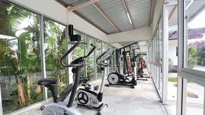 Un gimnasio con bicicletas estáticas y máquinas de pesas, amplias ventanas y suelo de hormigón.