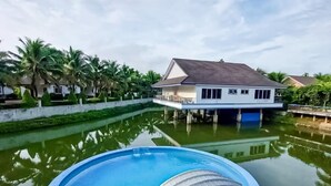 Una piscina con cubierta, una casa con techo de tejas y palmeras al fondo.