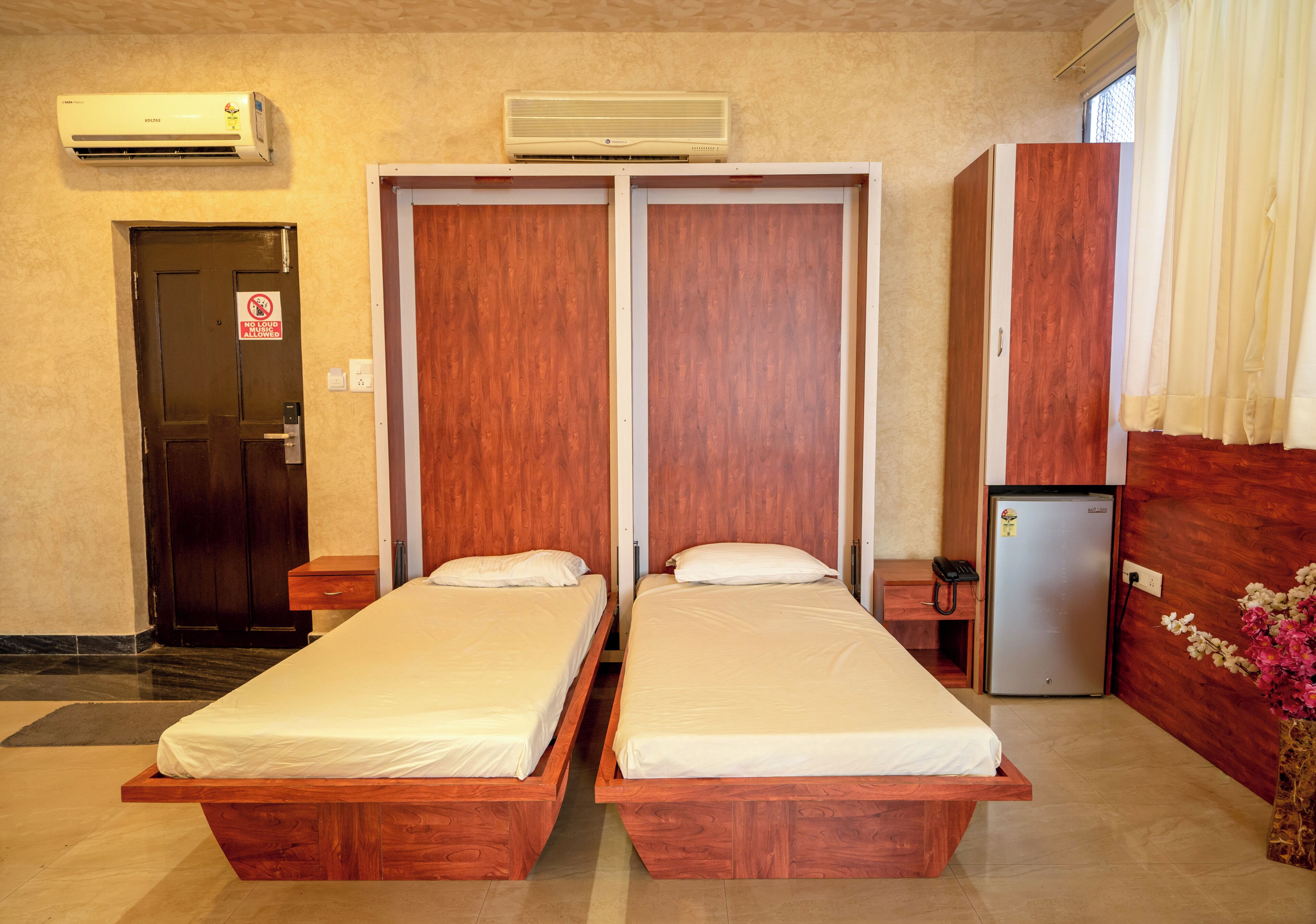 Une chambre d’hôtel avec deux lits simples, un minibar, un réfrigérateur et une porte sur laquelle est apposée une pancarte « Entrée interdite ».