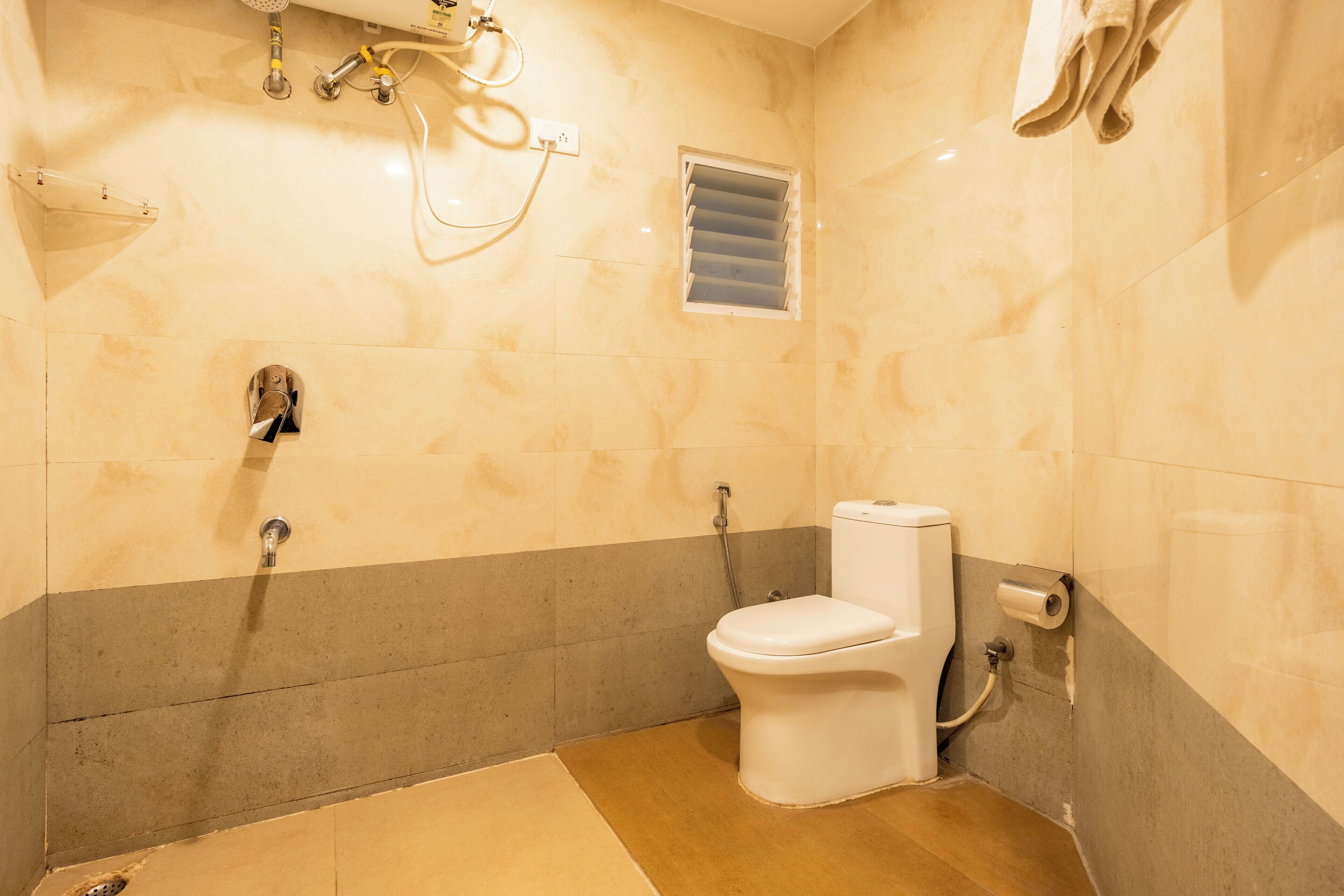 A bathroom with a toilet, shower, and a towel hanging on the wall.