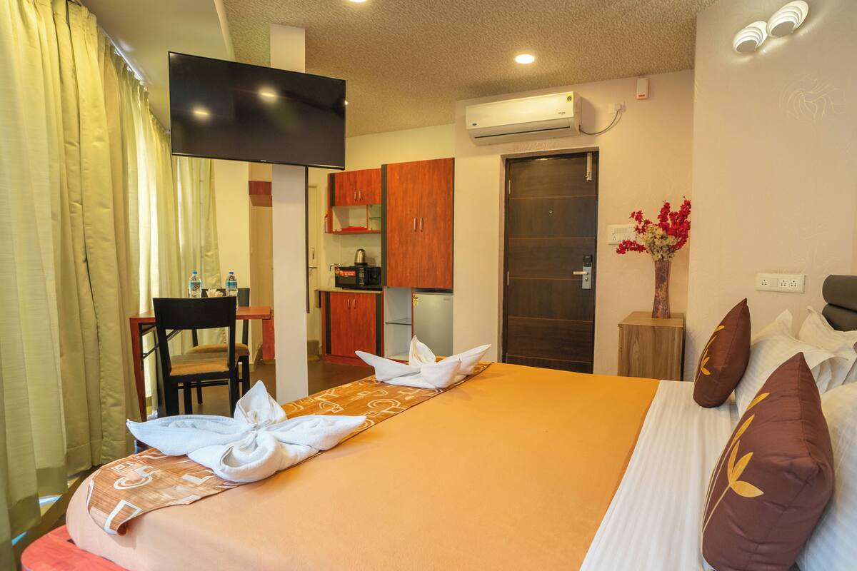 A hotel room with a bed, a TV, a kitchenette, and a bathroom.