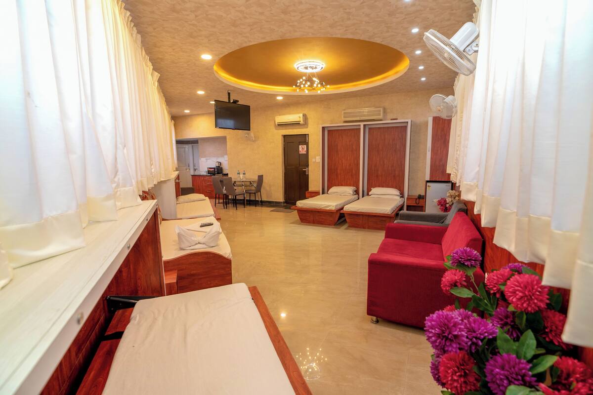A hotel room with a bed, a red sofa, a massage table, and a TV.