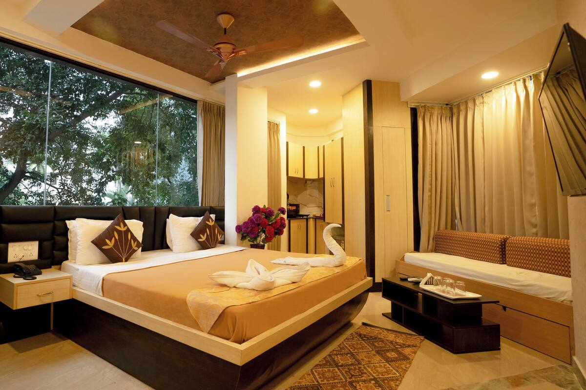 A modern hotel room with a large bed, a sitting area, and a view of trees through the window.