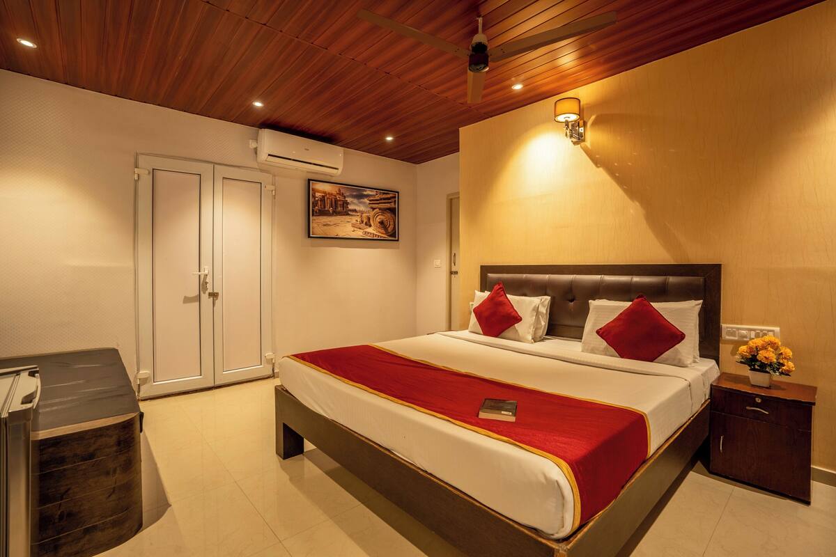 A hotel room with a large bed, a bedside table with a lamp, a wardrobe, and a ceiling fan.
