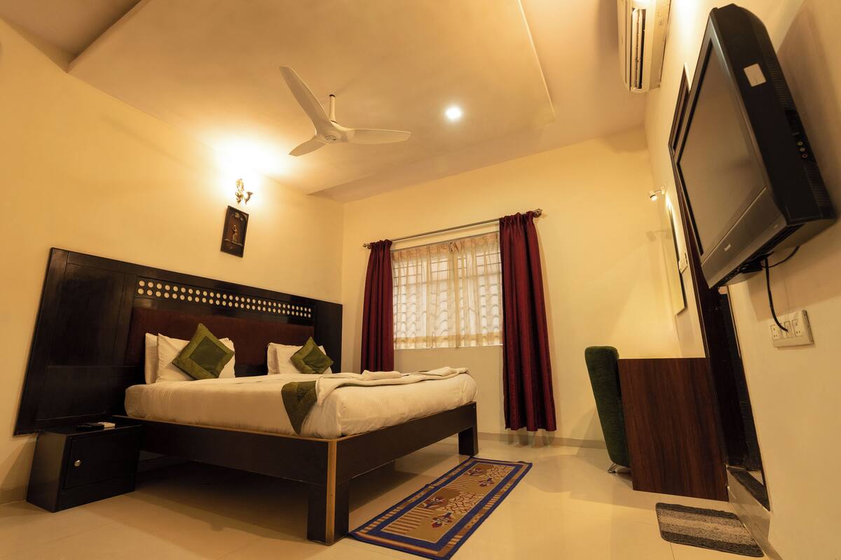 A bedroom with a bed, nightstand, ceiling fan, window with curtains, and a television.