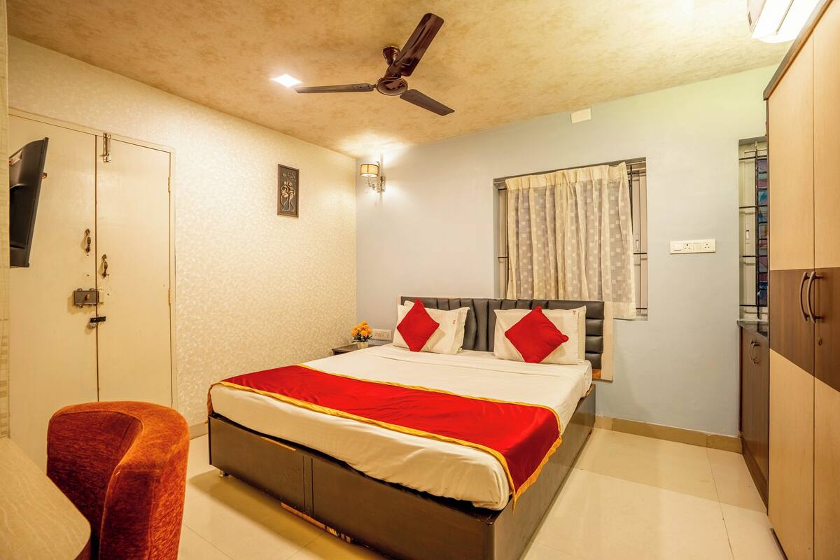 A bedroom with a bed, a chair, a wardrobe, a ceiling fan, and a window with curtains.