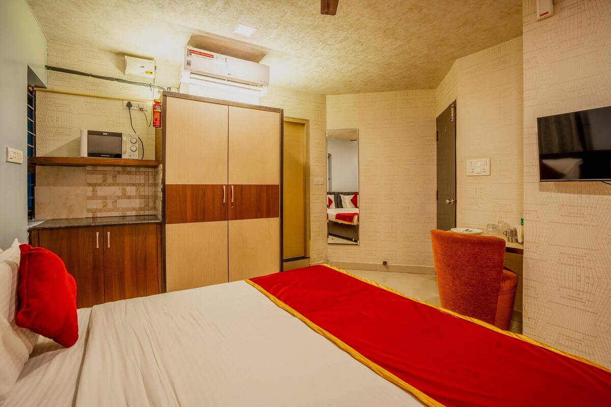 A hotel room with a bed, a red throw, a wooden wardrobe, a microwave, and a TV on the wall.