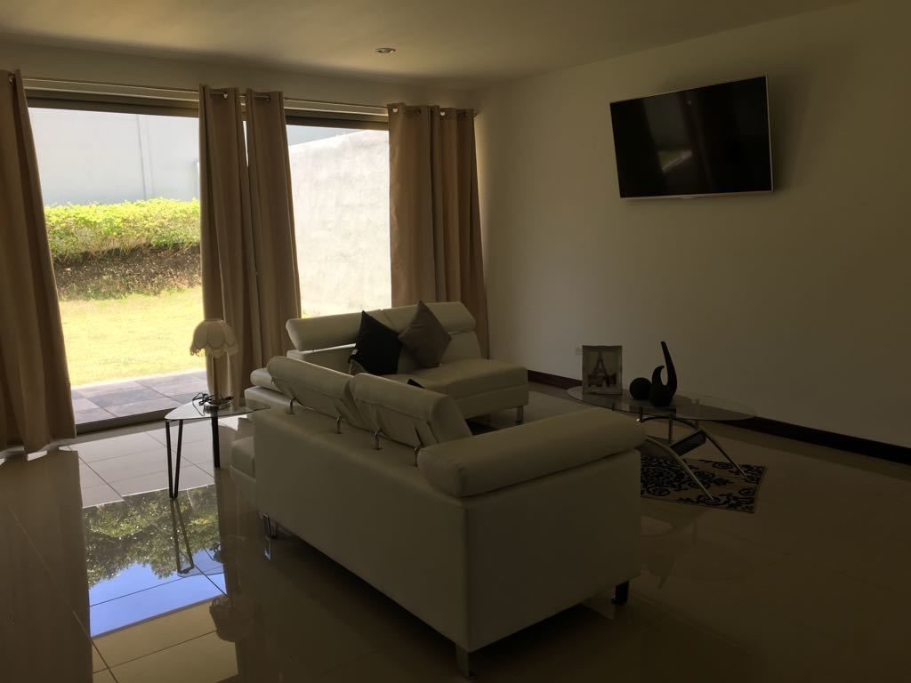 Una sala de estar moderna con un sofá blanco, una mesa de centro de vidrio y un televisor de pantalla plana montado en la pared.