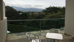 A balcony with two metal chairs and a table, overlooking a cityscape with mountains and trees. - Las Yagrumas Condo Escazu (San Rafael)