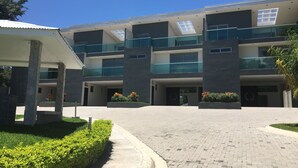 A modern multi-story building with a covered entrance, glass balconies, and landscaped areas. - Las Yagrumas Condo Escazu (San Rafael)