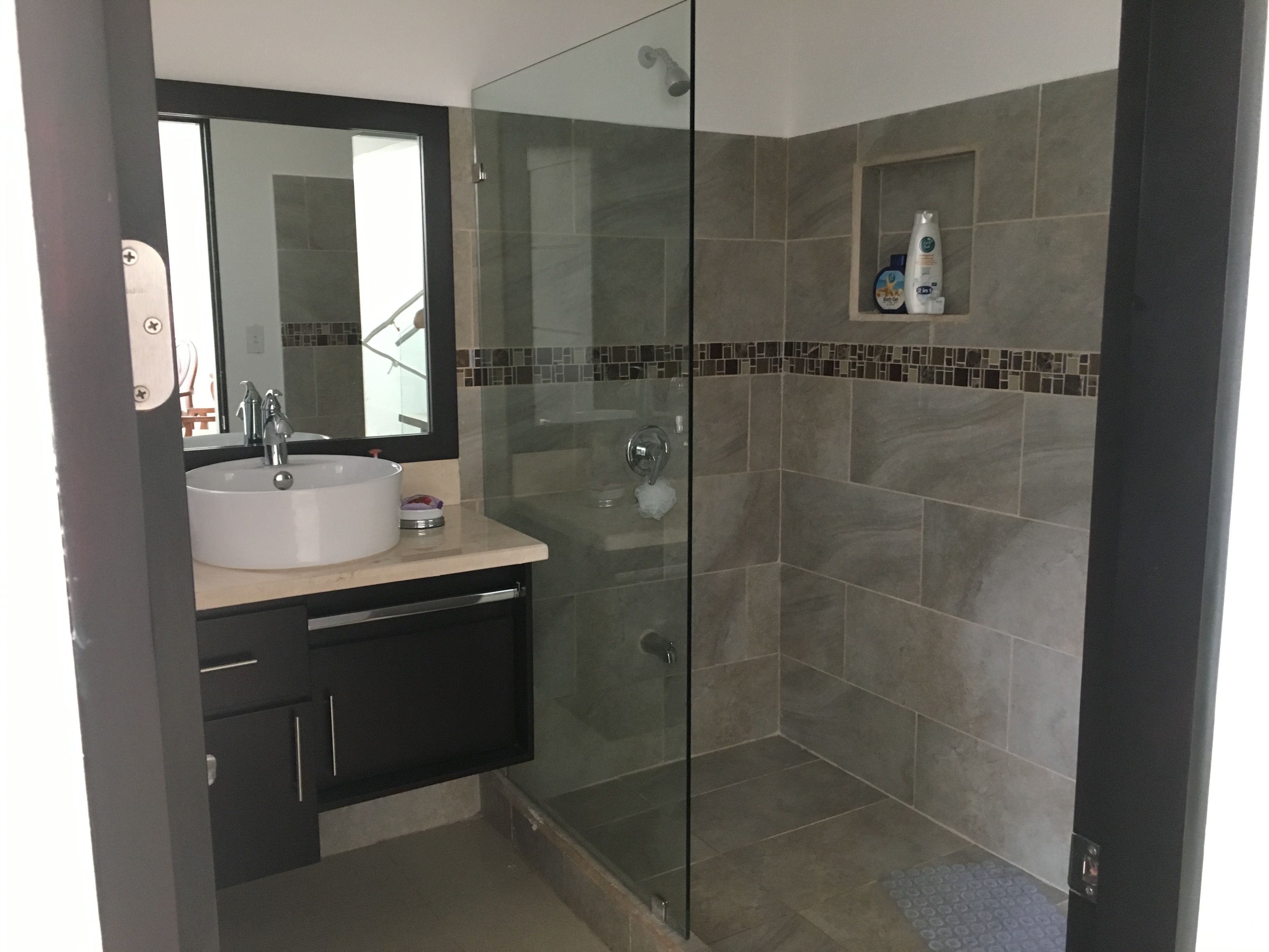 A modern bathroom with a glass-enclosed shower, a sink with a mirror, and a small shelf with toiletries.