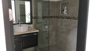 A modern bathroom with a glass-enclosed shower, a sink with a mirror, and a small shelf with toiletries.