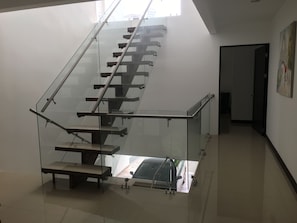 A modern staircase with glass railings and a metal handrail, leading to a landing with a view of a car outside.