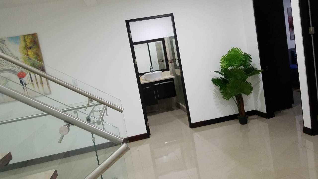 A modern interior with a glass railing, a potted plant, and a bathroom with a mirror and sink.