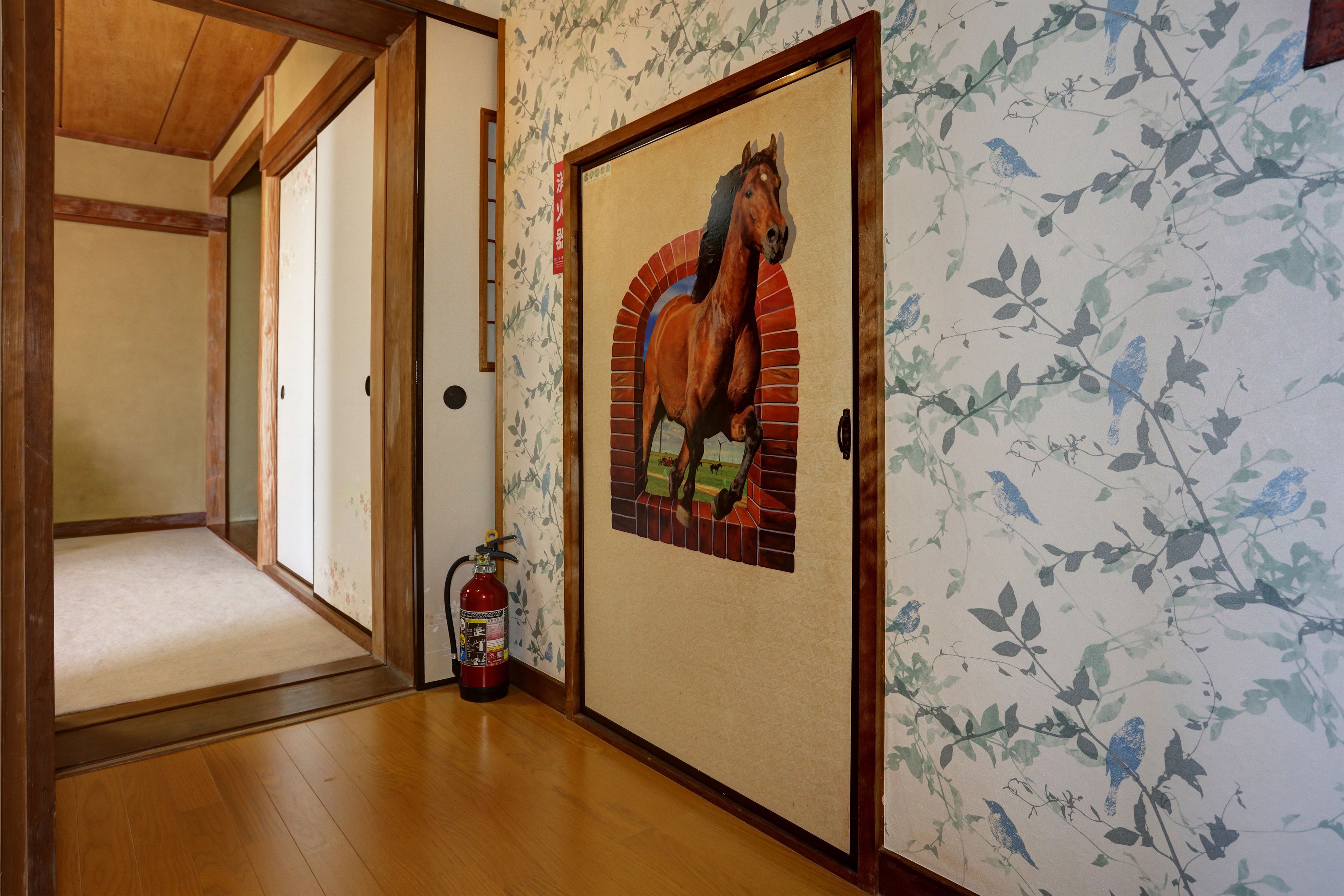 A hallway with wooden flooring, a fire extinguisher, and a door with a horse mural.