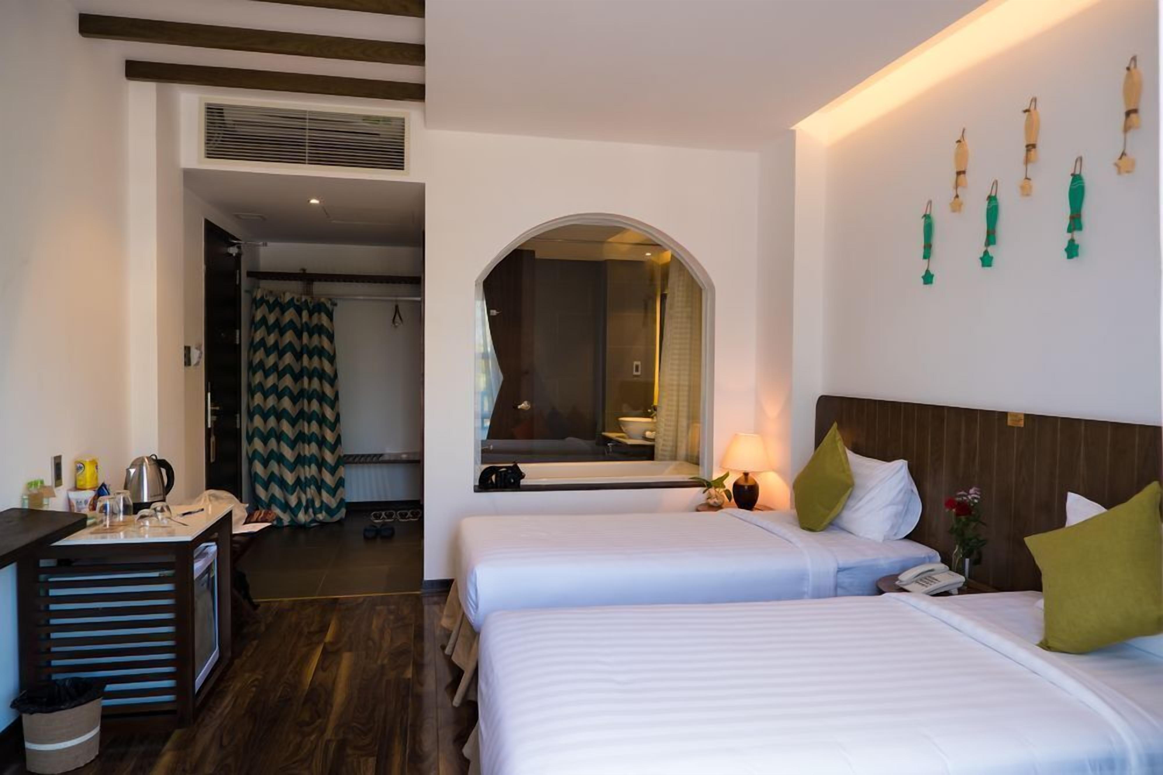 A hotel room with two beds, a desk, a mirror, and a shower area.
