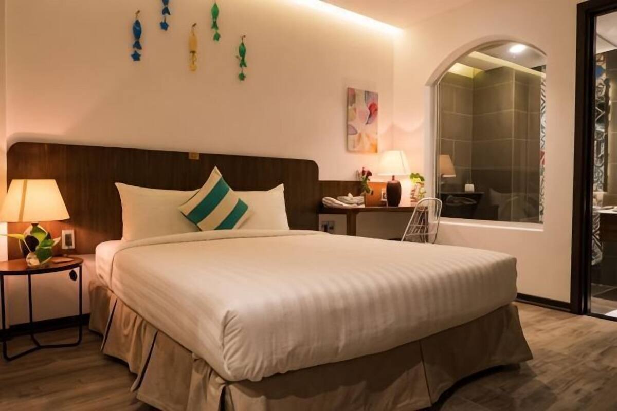Una habitación de hotel con cama, mesita de noche, lámpara y ventana con vistas.