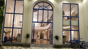 A hotel entrance with a stone-patterned floor, large glass doors with blue frames, and a staircase leading to an upper level. - Santori Hotel Danang Bay (Da Nang)
