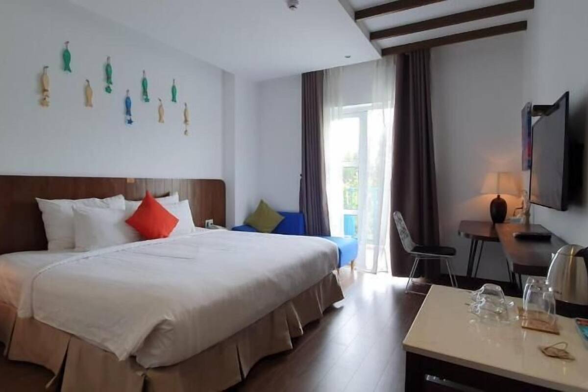 Habitación de hotel con una cama grande, un escritorio con hervidor, una silla y un televisor.