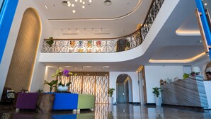 A modern hotel lobby with a curved ceiling, a reception desk, and a seating area with colorful sofas. - Santori Hotel Danang Bay (Da Nang)