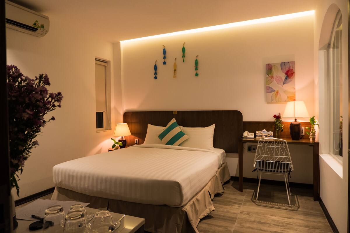 Una habitación de hotel con una cama grande, mesitas de noche, un escritorio, una silla y una ventana.